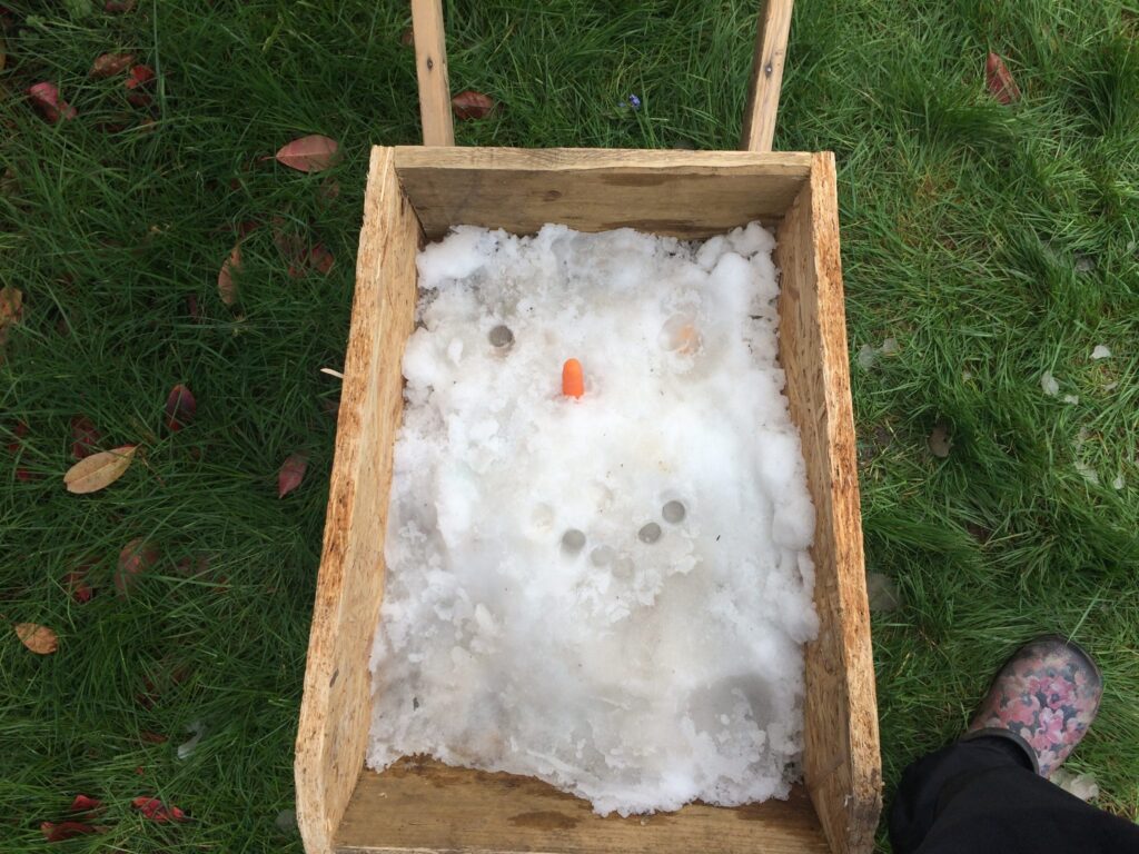 A wooden wheelbarrow filled with snow and finger holes used to make a face