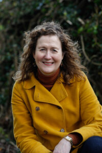 Photograph of Nicolette Evans outside wearing a mustard yellow coloured coat and brown top